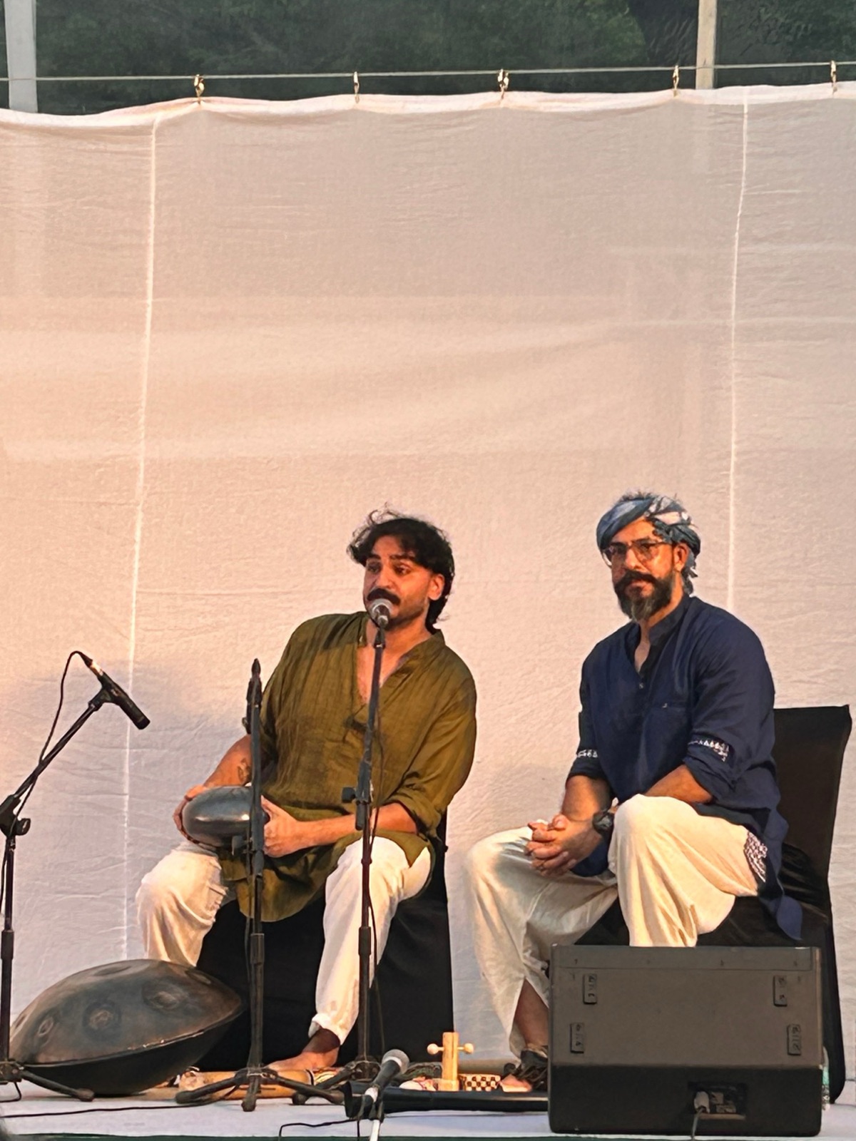 Ashim Bery on stage at Baarish, Travancore Palace, speaking at the microphone with a small steel drum, his handpan at his feet
