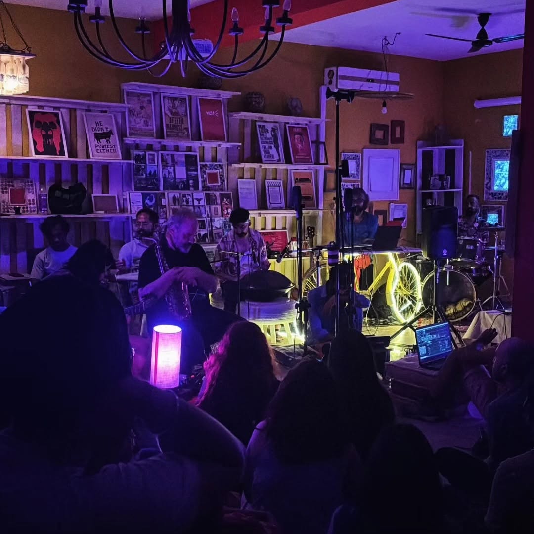 Ashim Bery at a handpan in a packed, dimly lit room, among an ensemble with a saxophonist, guitarist, keys and drums, the audience seated on the floor