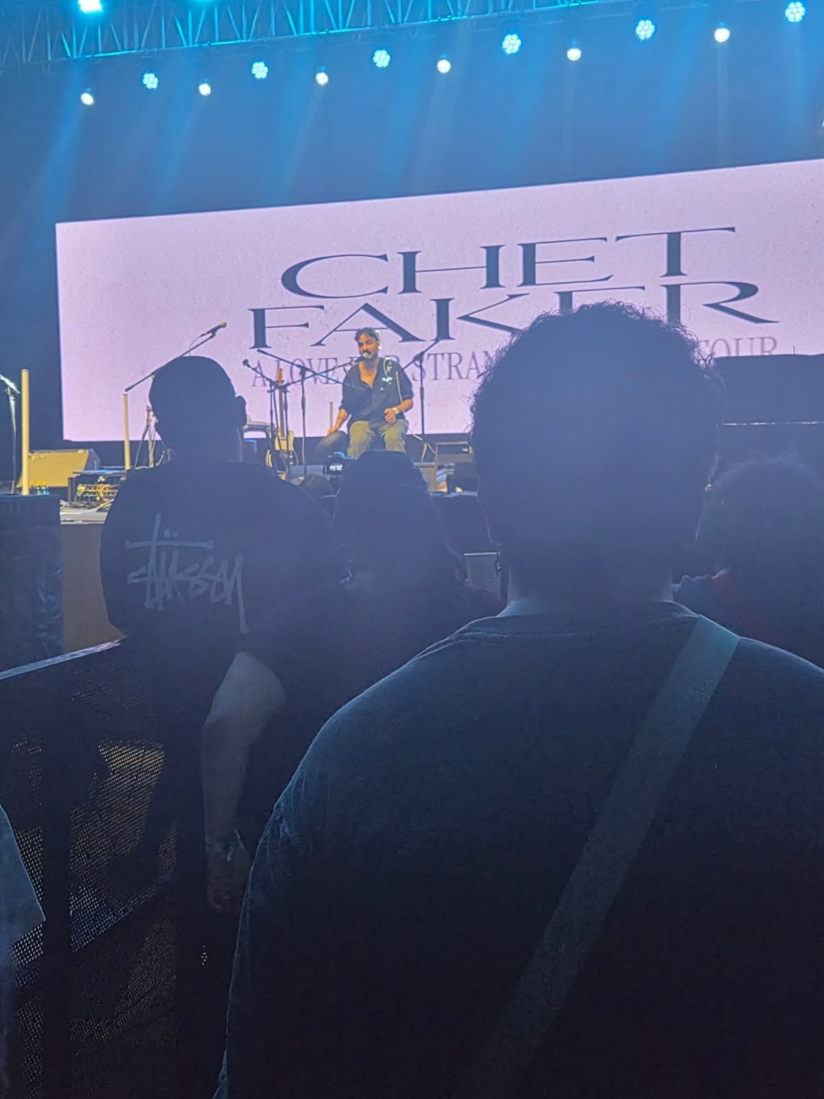 View from the crowd of Ashim Bery seated on stage, with the Chet Faker 'A Love For Strangers' tour screen behind him